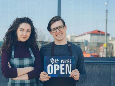 Fiche Google Business Profile : deux commerçants devant leur boutique avec un panneau ouvert