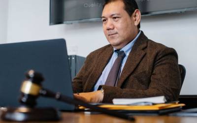 Avocat en costume sombre assis à son bureau devant un ordinateur portable, livres de droit en arrière-plan