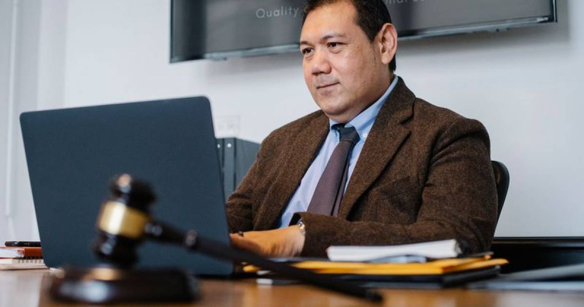 Avocat en costume sombre assis à son bureau devant un ordinateur portable, livres de droit en arrière-plan