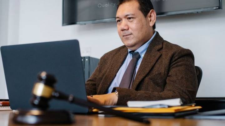 Avocat en costume sombre assis à son bureau devant un ordinateur portable, livres de droit en arrière-plan